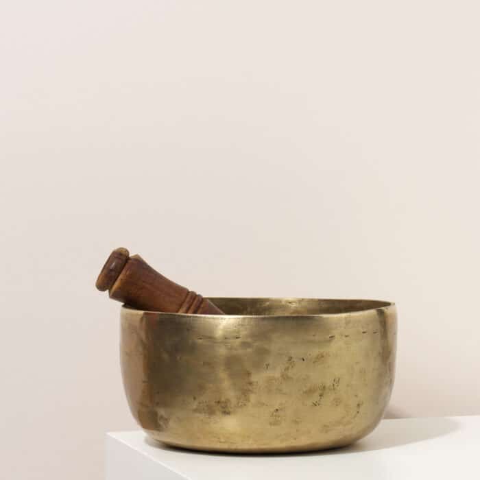Copper singing bowl and wooden clapper on a white table. Musical instrument for meditation, relaxation, various medical practices related to biorhythms, in yoga