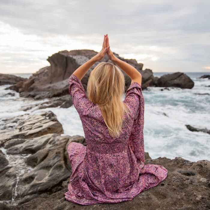 Girl meditates sitting on the rocks looking at the ocean and she does yoga, spirituality concept