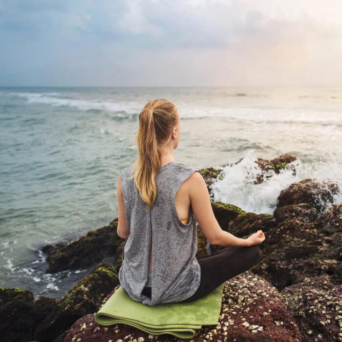 Woman meditate on the rock near the sea with wave splashes on sunset