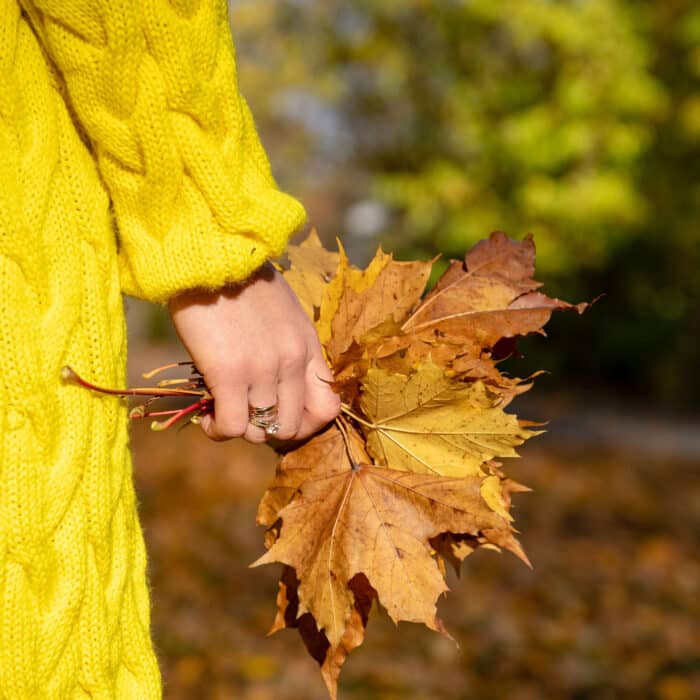 The woman in the yellow jacket holds colorful leaves in her hands.