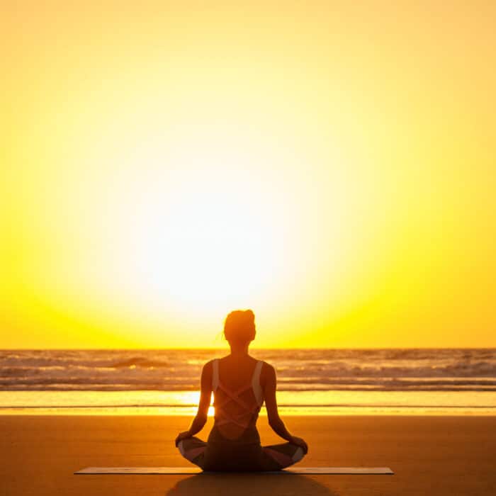 Silhouette of young woman in a stylish suit for yogi jumpsuit doing yoga on the beach in pose copy space.