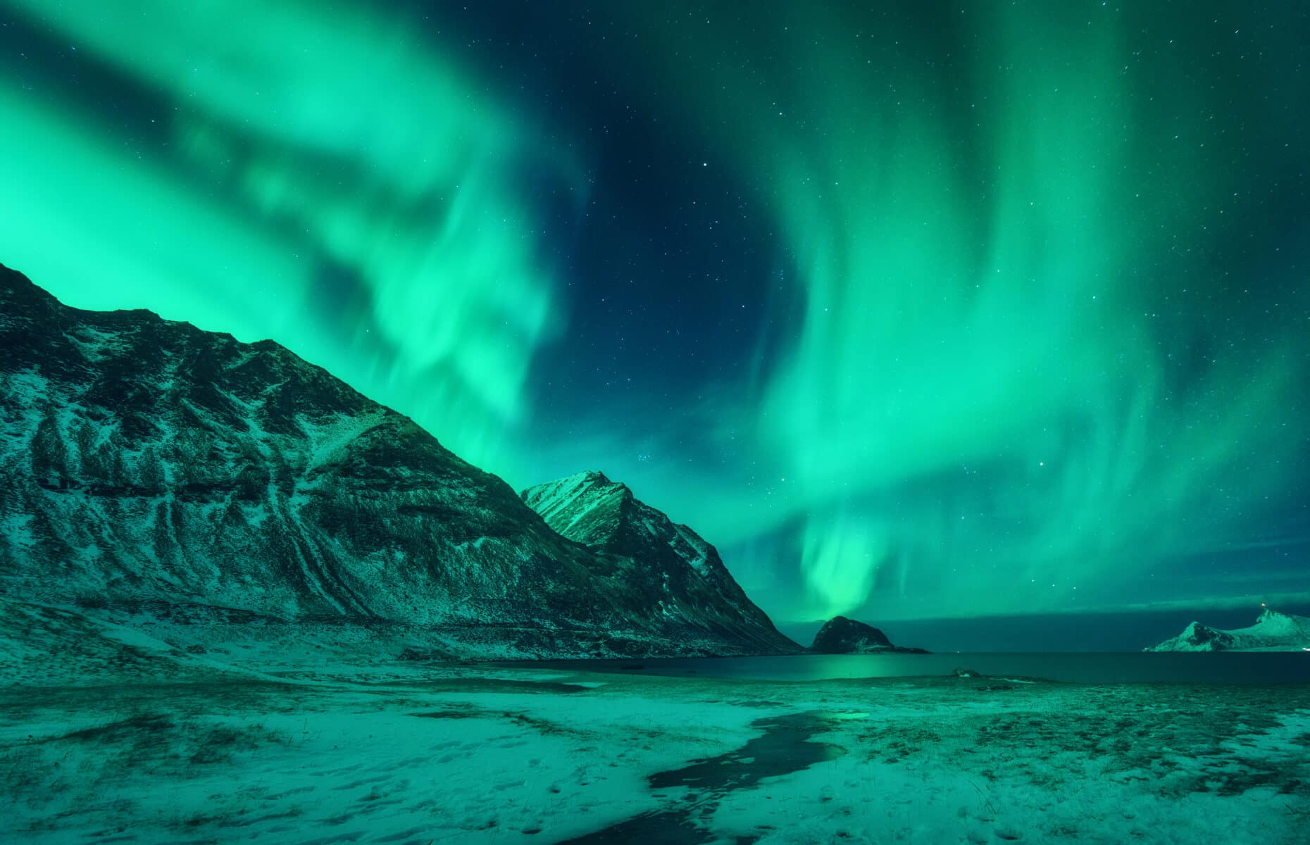 Northern lights in Lofoten islands, Norway. Green aurora borealis. Starry sky with polar lights. Night winter landscape with aurora, sea, high rocks, stream, nordic beach and snowy mountains. Travel