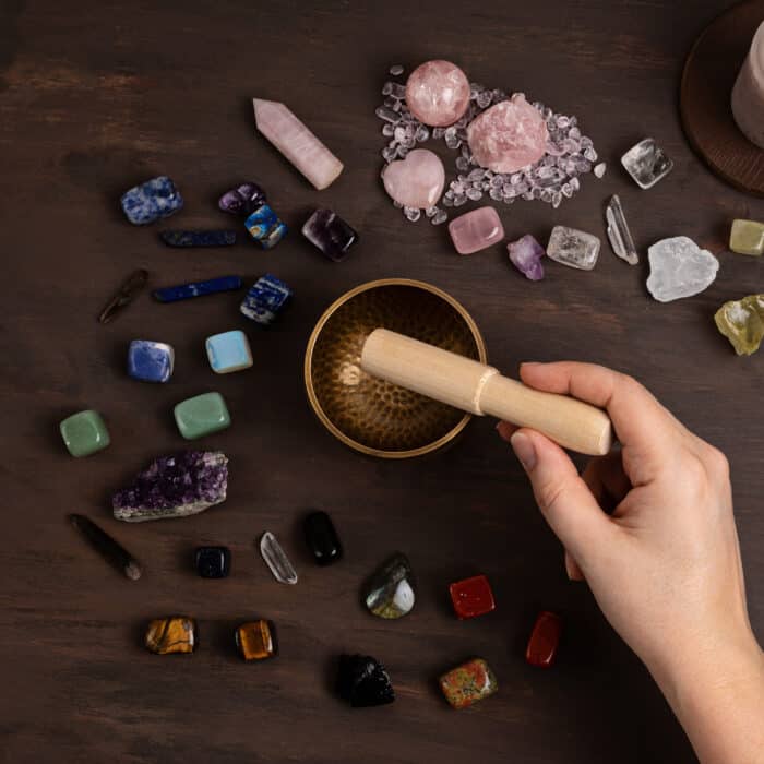 Woman cleansing healing chakra crystals with tibetan singing bowl. Rituals with gemstones and aromatherapy for wellness, healing, meditation, destress, relaxation, mental health, spiritual practices. Energetical power concept