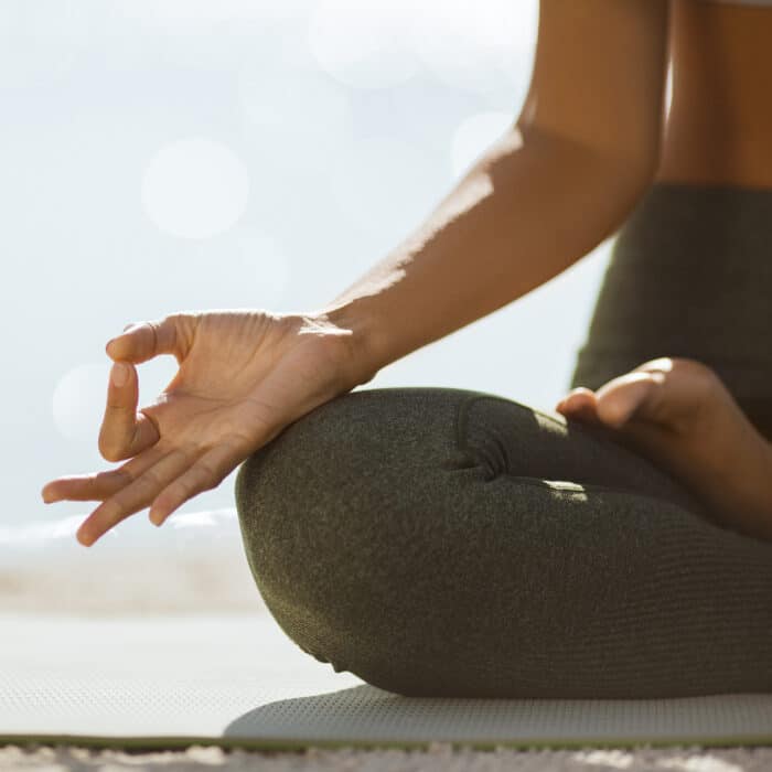 Woman meditation on the nature concept. Close-up view on hand. Sporty young woman meditating at the beach. Girl in sportswear practicing yoga on the beach. Shallow DOF copy space sea background. Music for meditation creative concept