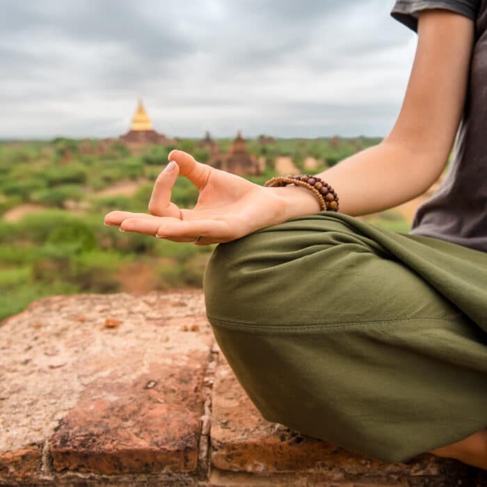 Woman with hands in Yoga mudra meditating on the top of pagoda at sunset in Myanmar, Bagan