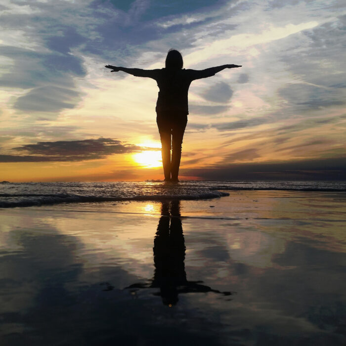 Silhoutte of a woman standing near water facing sunrise sunset