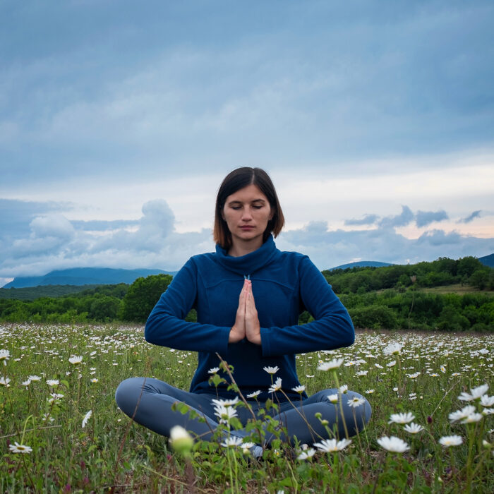 A young woman doing yoga in the field. Meditation in a chamomile field before sunset. Deep blue colours, calm and peaceful. Spiritual and emotional concept.